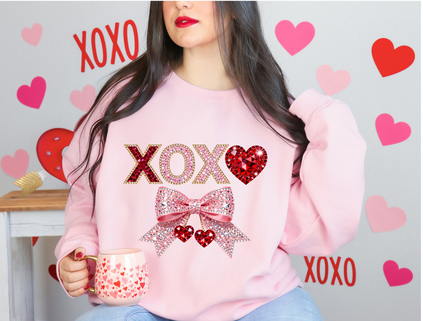 Person wearing a pink sweatshirt with 'XOXO' and heart designs, holding a mug with hearts,